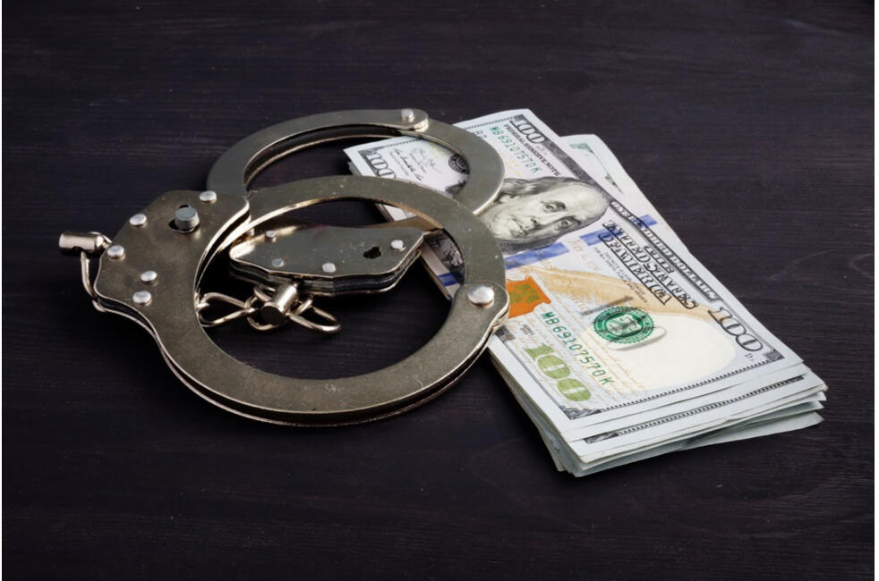 A pair of handcuffs on top of hundred dollar bills.