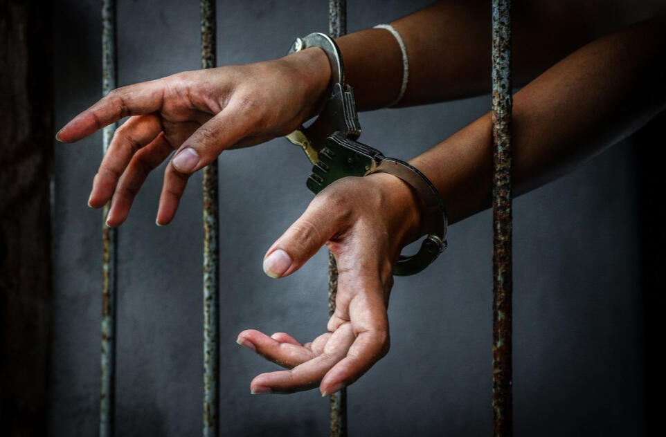 Person in jail with handcuffs on reaching through the bars.